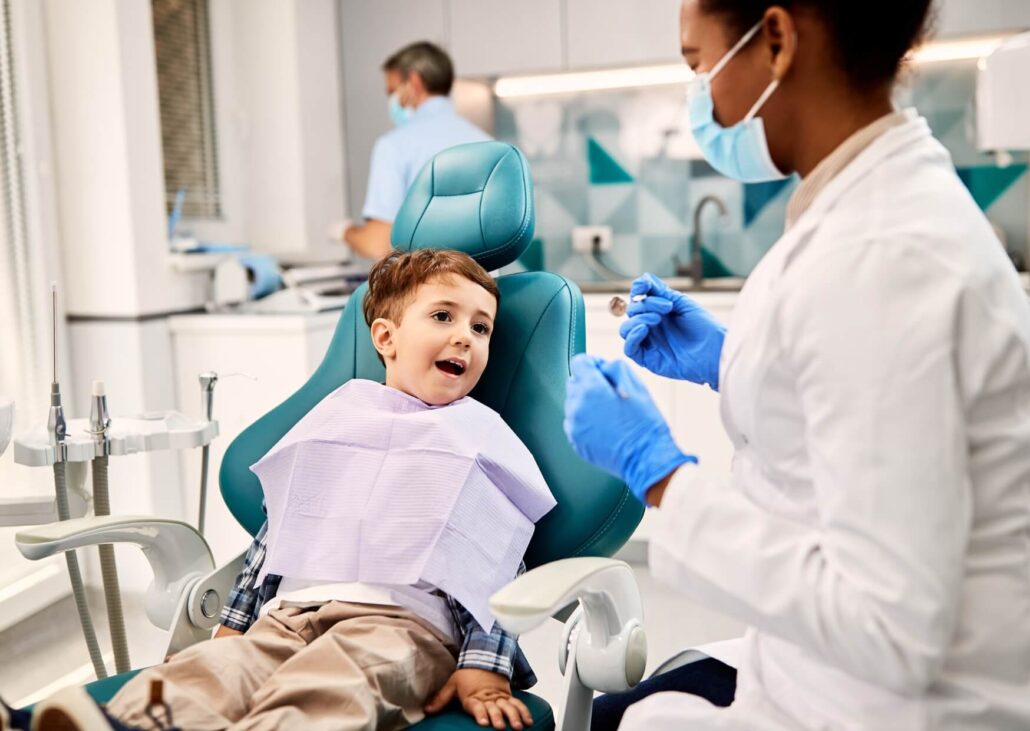 Young child talking with a pediatric dentist during an appointment to evaluate the need for a dental spacer after early tooth loss.