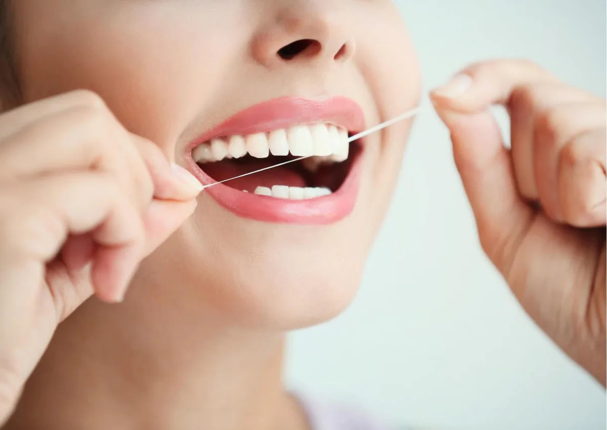 Woman flossing her teeth to maintain oral hygiene and support the long-term lifespan of dental implants.