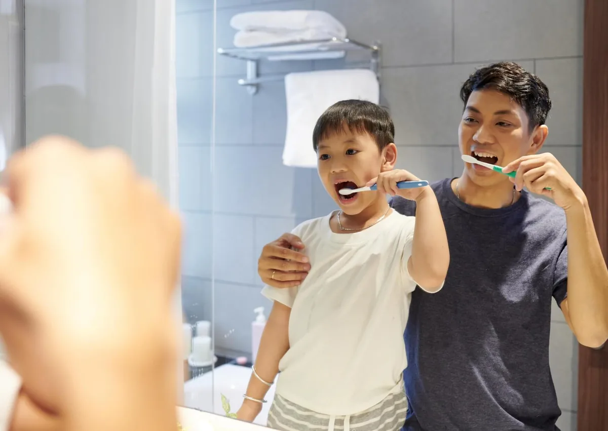 Parent and child brushing their teeth together to support healthy teeth as children grow.