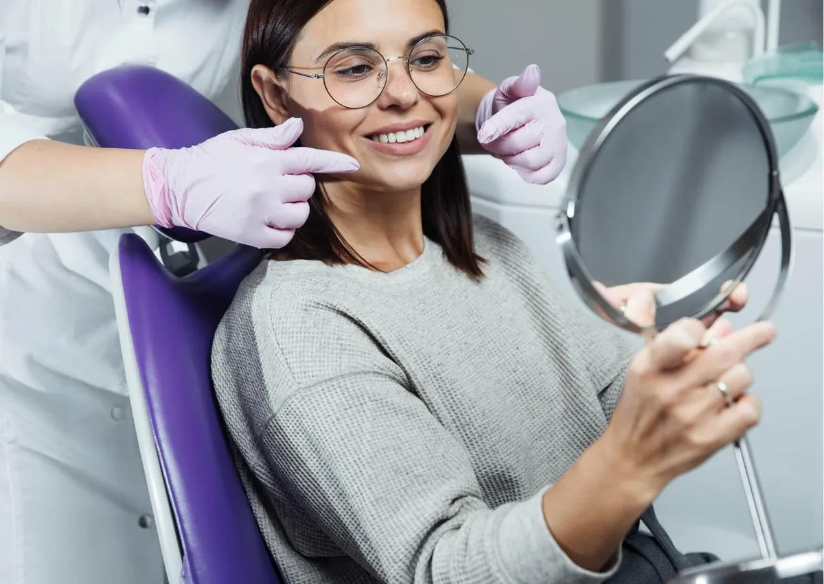 Patient viewing her brighter smile in a mirror after professional teeth whitening treatment.