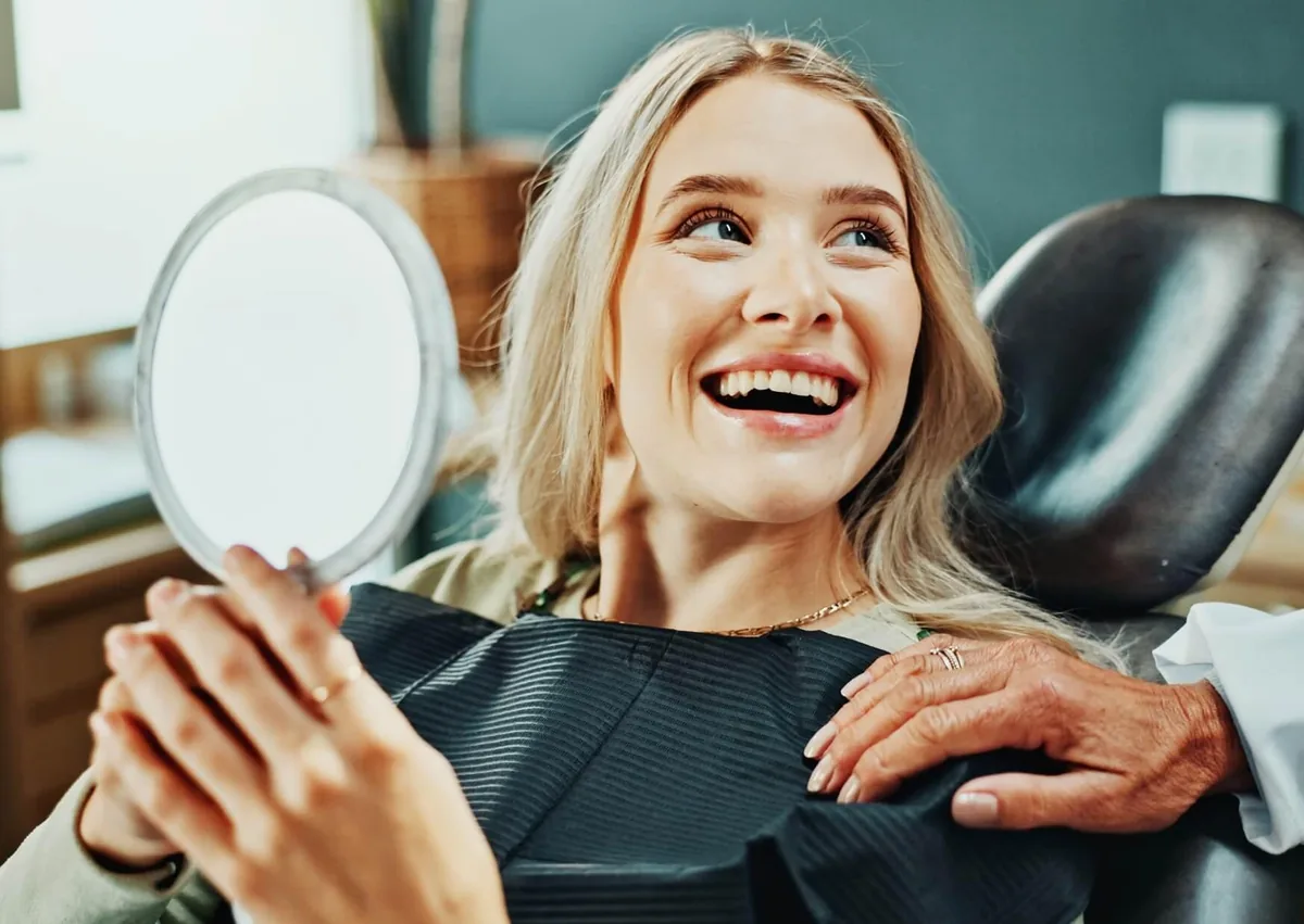 Patient smiling at her reflection after completing a smile makeover at a dental office.